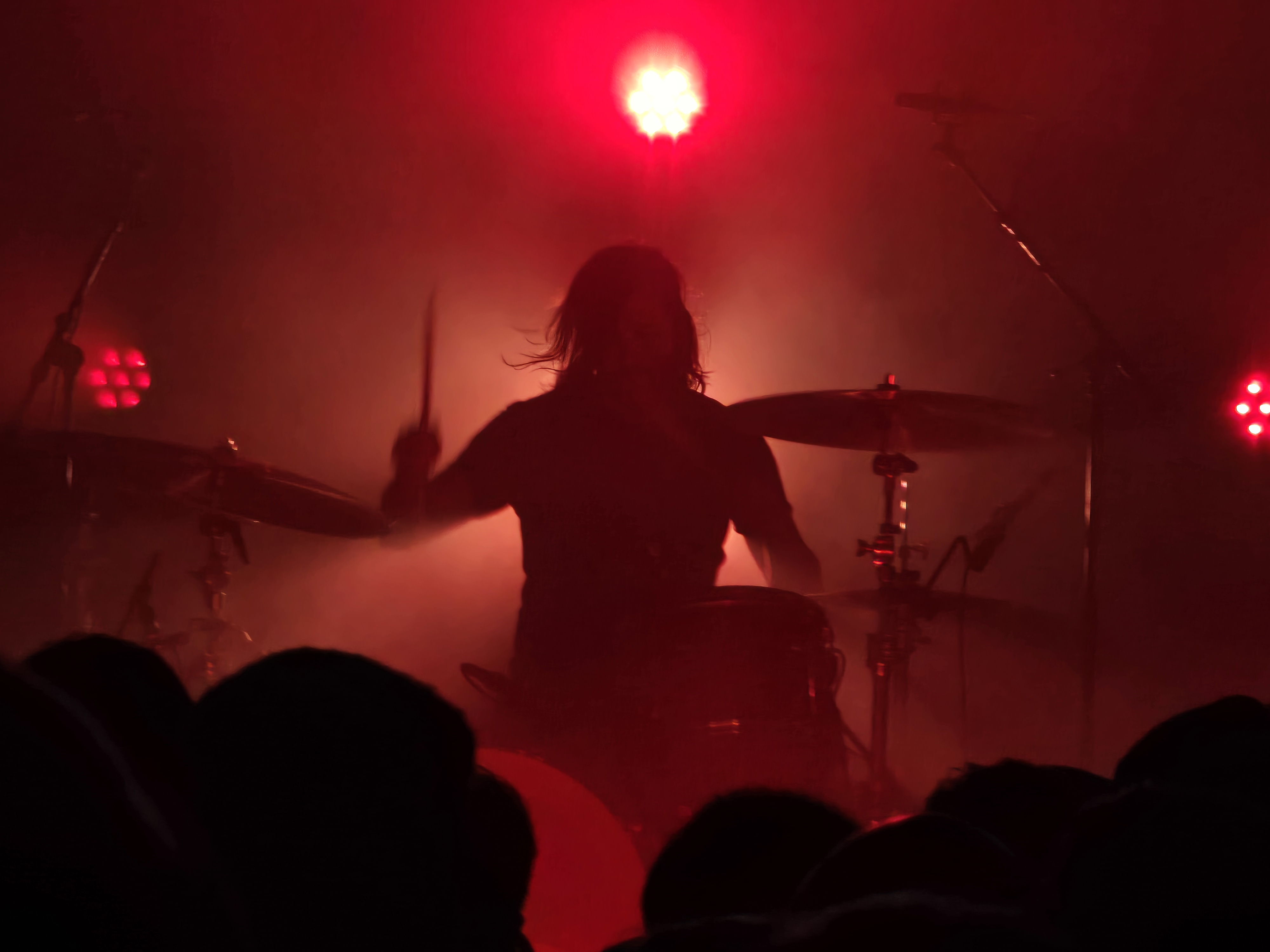 The silhouetted form of a drummer, bathed in red backlight. 
