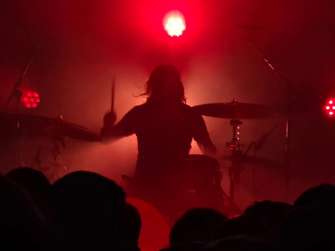 The silhouetted form of a drummer, bathed in red backlight. 